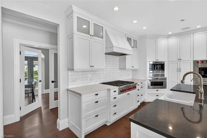 Kitchen with dark stone countertops, white cabinets, glass insert cabinets, french doors, and recessed lighting