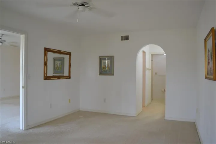 Empty room featuring a ceiling fan, arched walkways, and light carpet