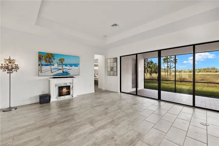 Tray ceiling, fireplace with marble-look surround, large format tile flooring, and expansive sliding glass doors opening to a screened lanai with a tiled floor