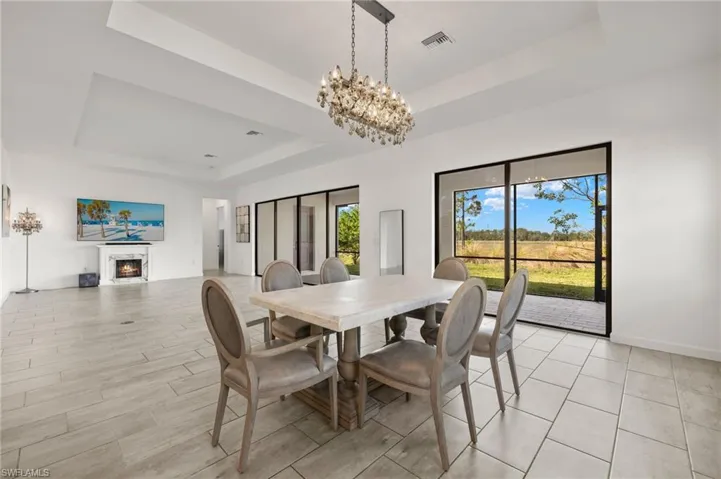 Tray ceiling with a crystal chandelier, large format tile flooring, and a fireplace with a marble surround