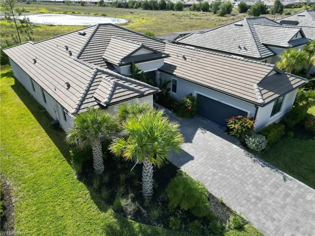 Contemporary residence featuring a paved driveway, attached garage, tile roof, and mature landscaping