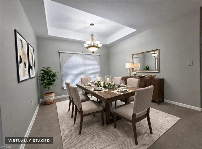 Tray ceiling with an elegant chandelier, tiled flooring, and window blinds