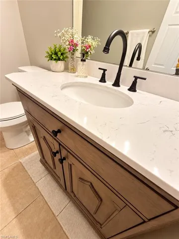 New vanity and plumbing w/Wood-finish vanity with black hardware, white countertop with integrated sink, black wall-mounted faucet, and tile flooring