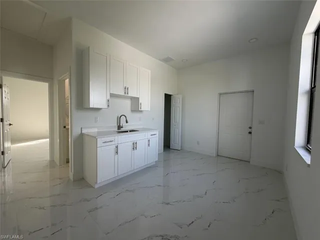 White cabinetry with brushed nickel hardware, undermount sink with gooseneck faucet, light-toned countertop, and recessed lighting