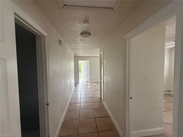 Corridor with a textured ceiling, tile patterned floors, and a textured wall