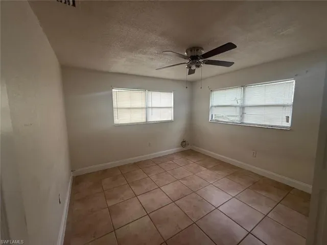 Empty room with a textured ceiling, light tile patterned floors, and ceiling fan