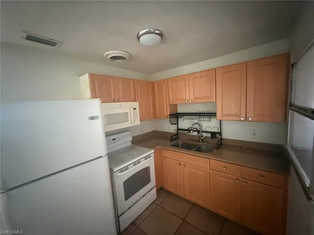 Kitchen featuring white appliances, dark tile patterned floors, and light brown cabinets