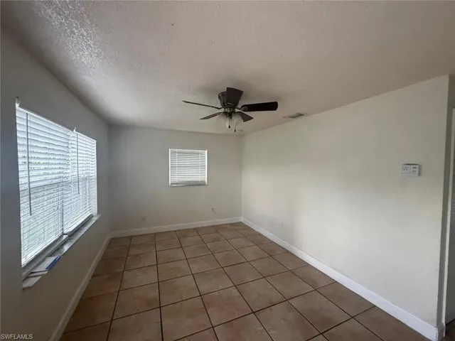 Tiled empty room with a textured ceiling, healthy amount of natural light, and a ceiling fan