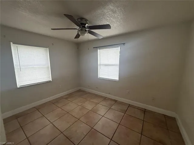 Empty room featuring a textured ceiling, light tile patterned floors, and a ceiling fan