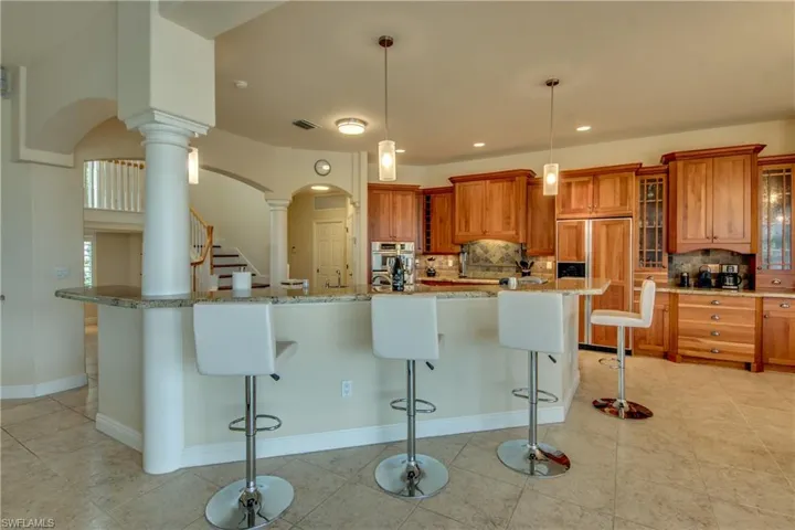 Kitchen featuring brown cabinets, arched walkways, paneled refrigerator, a breakfast bar area, and glass insert cabinets