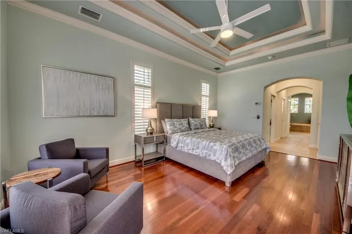 Bedroom featuring ornamental molding, arched walkways, hardwood / wood-style floors, multiple windows, and a raised ceiling