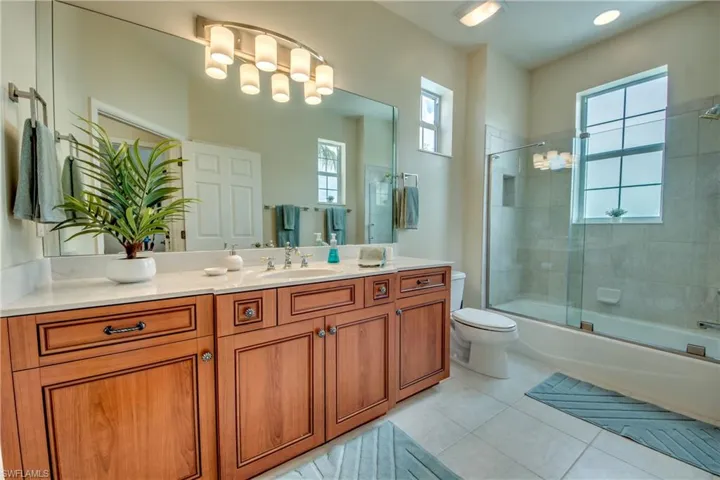 Bathroom with vanity, shower / bath combination with glass door, light tile patterned flooring, and healthy amount of natural light