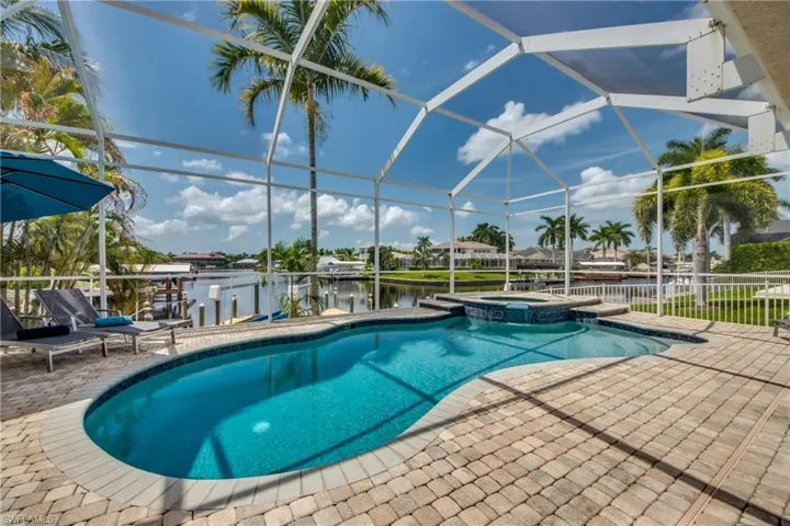 View of pool featuring a lanai, a water view, a pool with connected hot tub, a sunroom, and a patio area