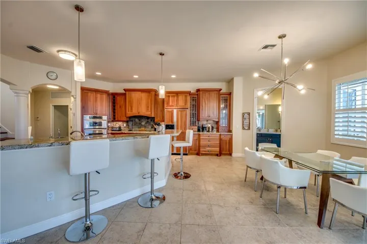 Kitchen with brown cabinets, glass insert cabinets, a breakfast bar, tasteful backsplash, and arched walkways
