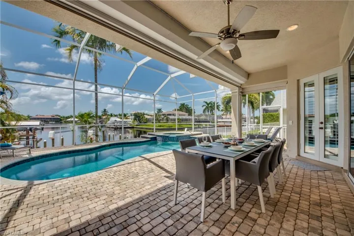 View of pool featuring a patio area, glass enclosure, a sunroom, a pool with connected hot tub, and a water view