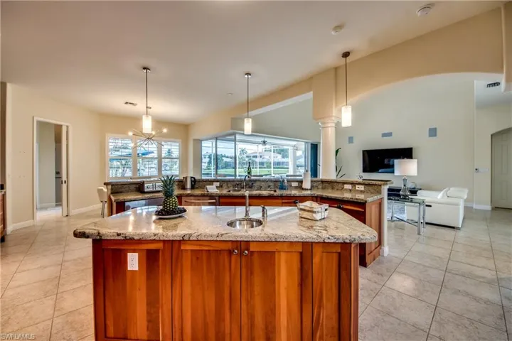 Kitchen featuring open floor plan, light stone counters, hanging light fixtures, brown cabinetry, and healthy amount of natural light