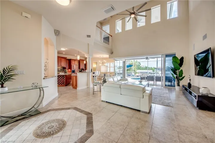 Living room with ceiling fan, inlaid floor details, light tile patterned floors, and arched walkways