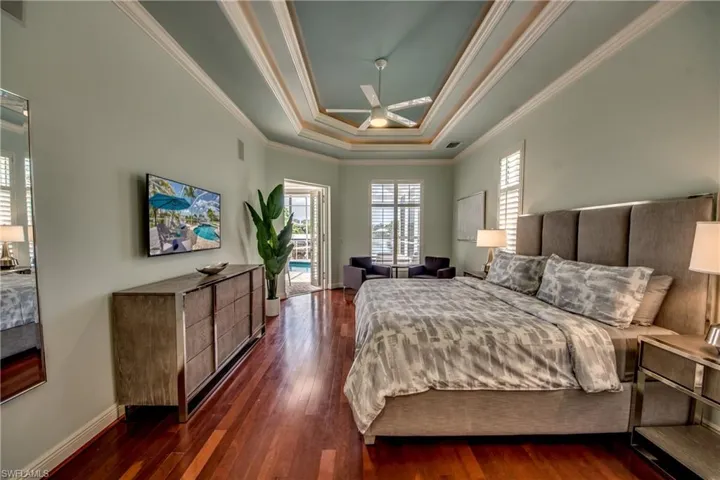 Bedroom featuring a tray ceiling, access to outside, ornamental molding, dark wood finished floors, and ceiling fan