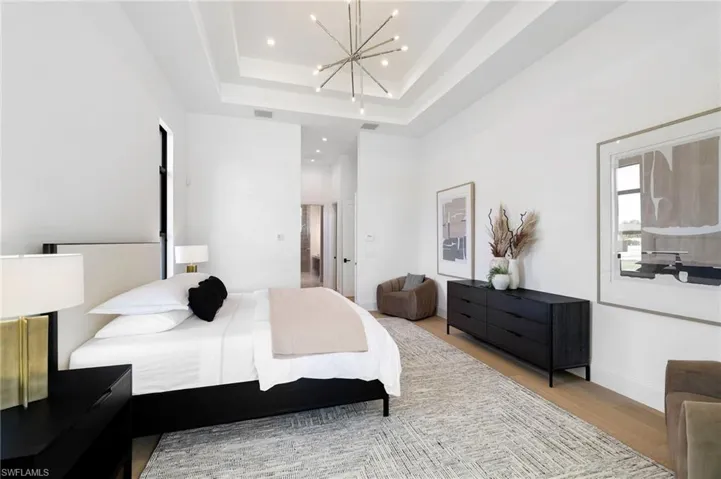 Bedroom with access to outside, wood finished floors, suspended lighting, and a tray ceiling