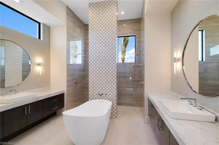 Bathroom featuring a walk in shower, two vanities, a freestanding bath, and plenty of natural light