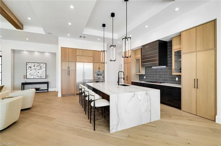 Dual tone kitchen with modern cabinets, light wood finished floors, hanging light fixtures, light stone counters, and a kitchen breakfast bar