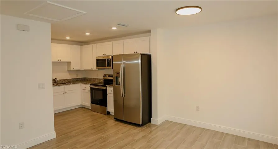 Kitchen featuring white cabinetry, stainless steel appliances, granite countertops, recessed lighting, and wood-finish flooring