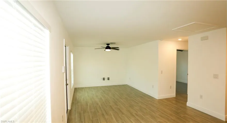 Spacious living area featuring wood-finish flooring, a contemporary ceiling fan with integrated lighting, and multiple windows with blinds