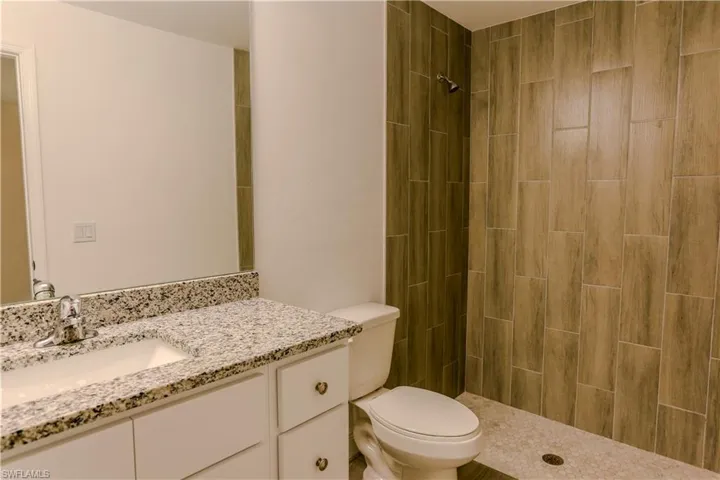 Bathroom featuring a walk-in shower with wood-look plank tiling, a white vanity with a speckled countertop, and an undermount sink