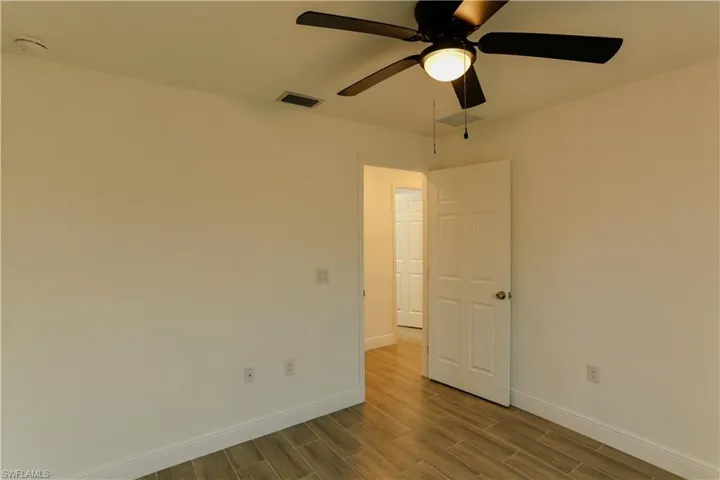 Interior space featuring wood-finish flooring, white walls, and a ceiling fan with integrated lighting