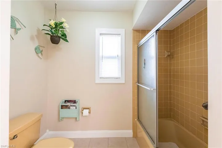Bathroom featuring toilet, tile patterned flooring, and enclosed tub / shower combo