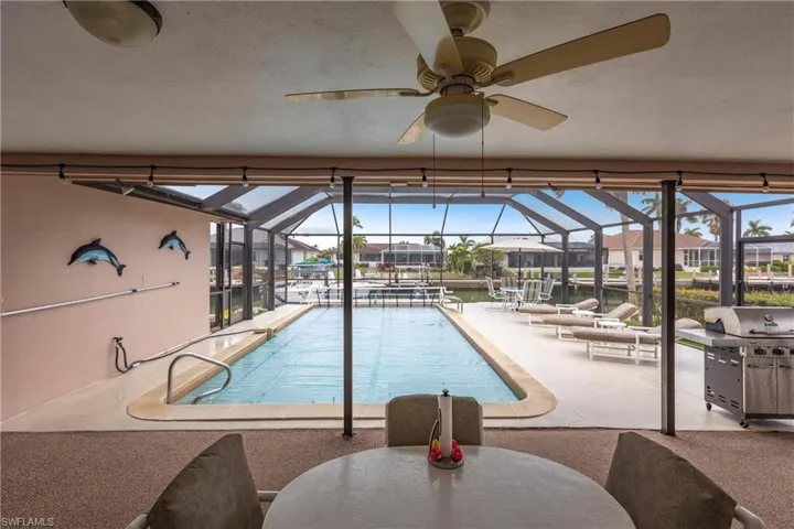 View of pool featuring glass enclosure, a patio area, a water view, and ceiling fan