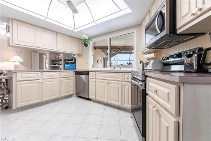 Kitchen featuring kitchen peninsula, appliances with stainless steel finishes, sink, light tile patterned flooring, and a skylight