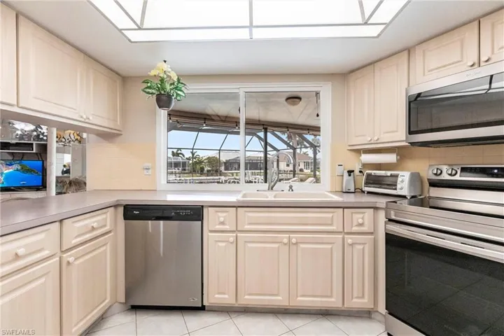 Kitchen featuring decorative backsplash, sink, appliances with stainless steel finishes, and light tile patterned flooring