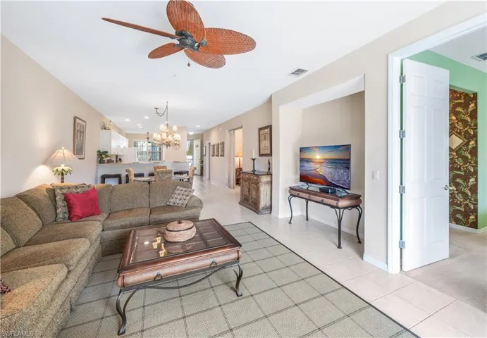Living room with light tile patterned floors, baseboards, visible vents, and ceiling fan with notable chandelier