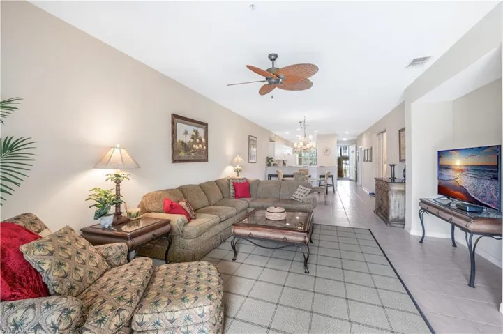 Living room with tile patterned floors, visible vents, baseboards, and ceiling fan with notable chandelier