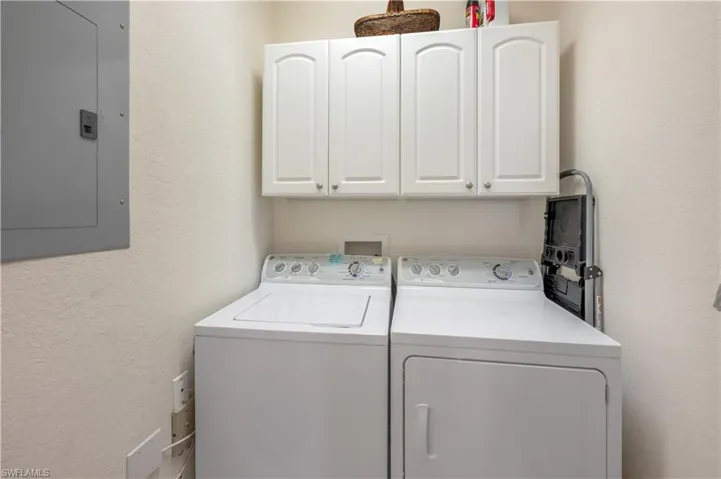 Laundry room with cabinet space, electric panel, a textured wall, and washing machine and clothes dryer