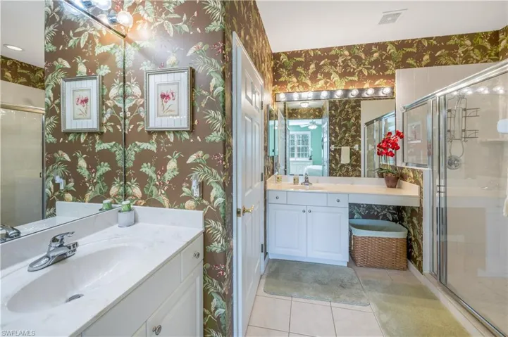 Full bath featuring a shower stall, two vanities, a sink, and wallpapered walls