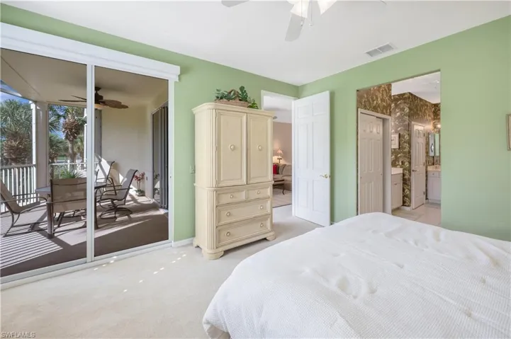Bedroom featuring light carpet, visible vents, ceiling fan, ensuite bathroom, and access to outside