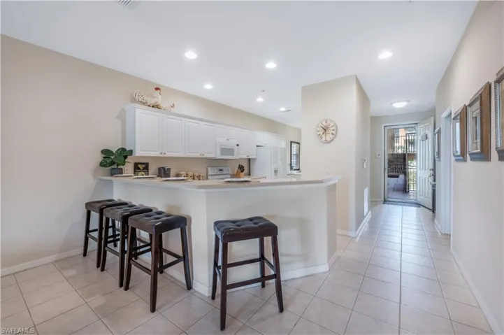 Kitchen featuring a peninsula, white appliances, white cabinets, and a kitchen breakfast bar
