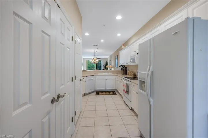 Kitchen featuring white appliances, light tile patterned floors, white cabinetry, a sink, and recessed lighting