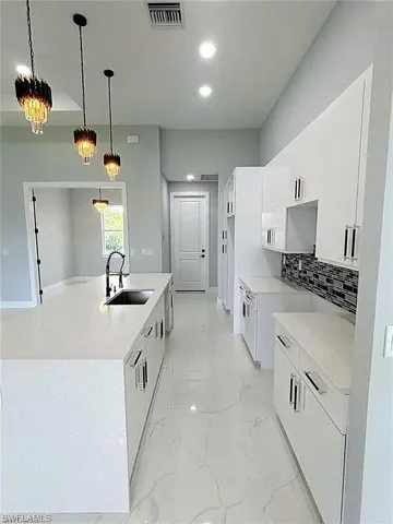 Kitchen featuring white cabinetry, pendant lighting, sink, and a center island with sink