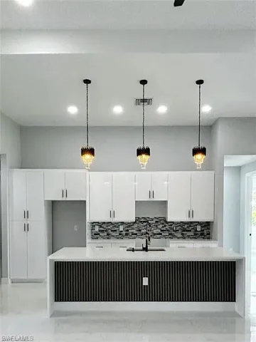 Kitchen featuring backsplash, decorative light fixtures, and white cabinets