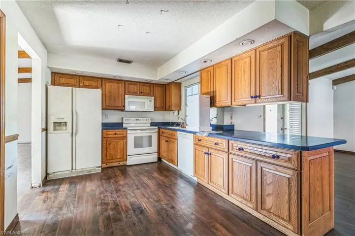 Kitchen featuring kitchen peninsula, a textured ceiling, dark wood-type flooring, sink, and white appliances