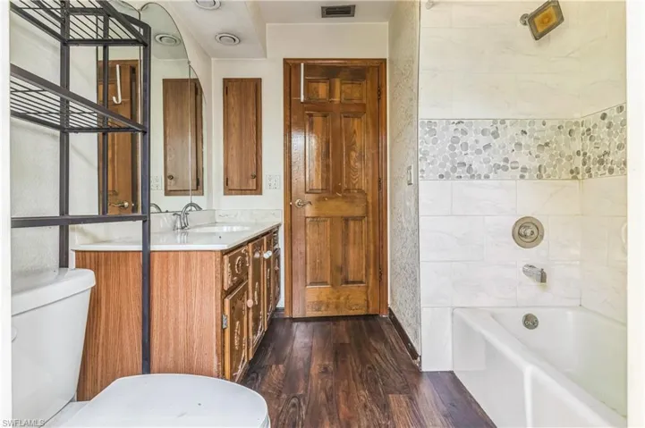 Full bathroom with wood-type flooring, tile walls, toilet, vanity, and tiled shower / bath combo
