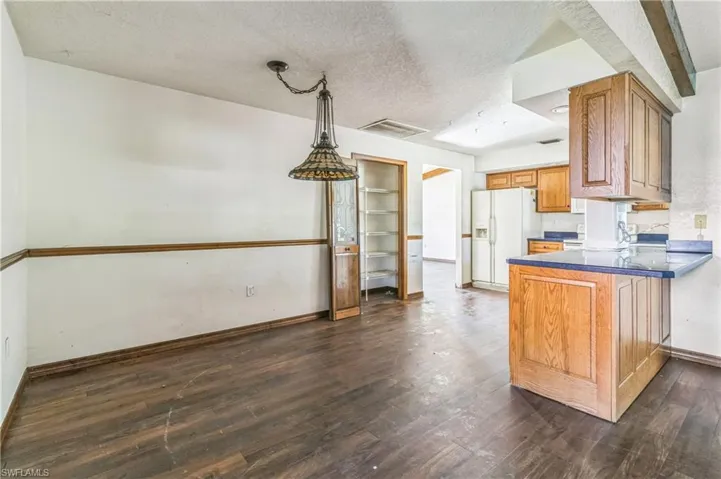 Kitchen featuring dark wood-type flooring, white fridge with ice dispenser, a textured ceiling, and kitchen peninsula