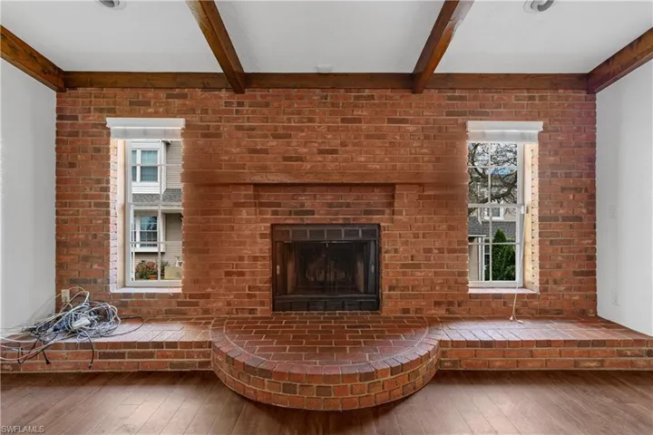 Unfurnished room featuring beam ceiling, a brick fireplace, and hardwood / wood-style floors