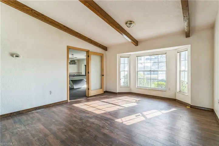 Unfurnished room featuring dark hardwood / wood-style flooring and vaulted ceiling with beams