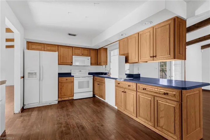 Kitchen with sink, kitchen peninsula, white appliances, and dark hardwood / wood-style flooring