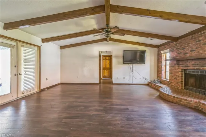 Unfurnished living room featuring a fireplace, dark hardwood / wood-style floors, lofted ceiling with beams, a textured ceiling, and ceiling fan