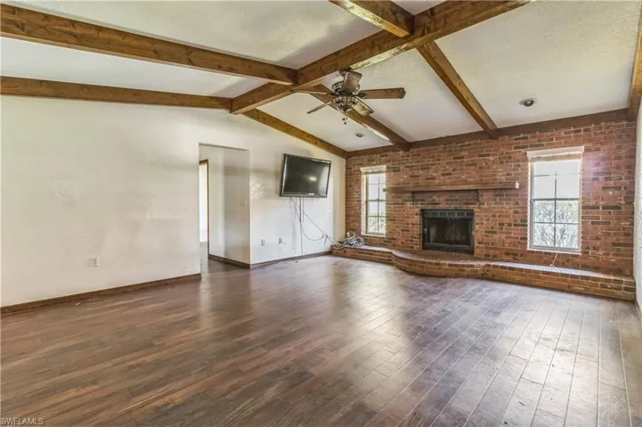 Unfurnished living room with a textured ceiling, vaulted ceiling with beams, a brick fireplace, and dark hardwood / wood-style flooring
